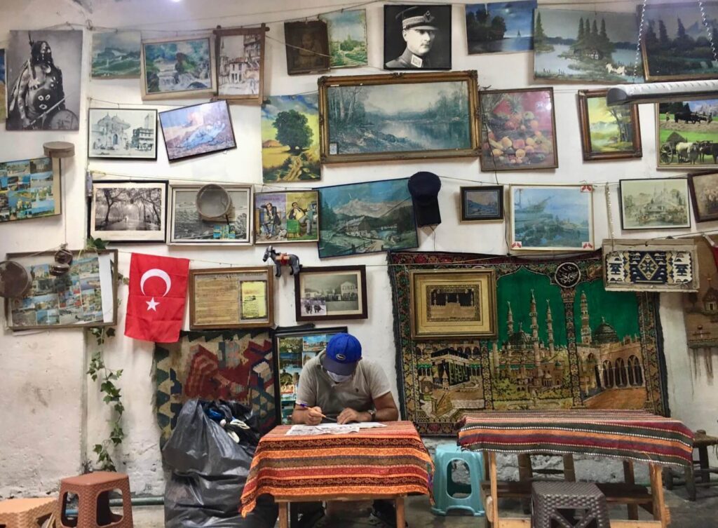Eminönü'nde tablo dolu duvarlar altında masada çalışan adam, Türk bayrağı ve Atatürk portresi
