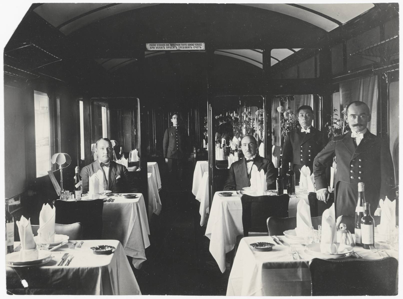 Orient Express vagonunda beyaz örtülü masalar, garsonlar ve yemekteki yolcular siyah-beyaz